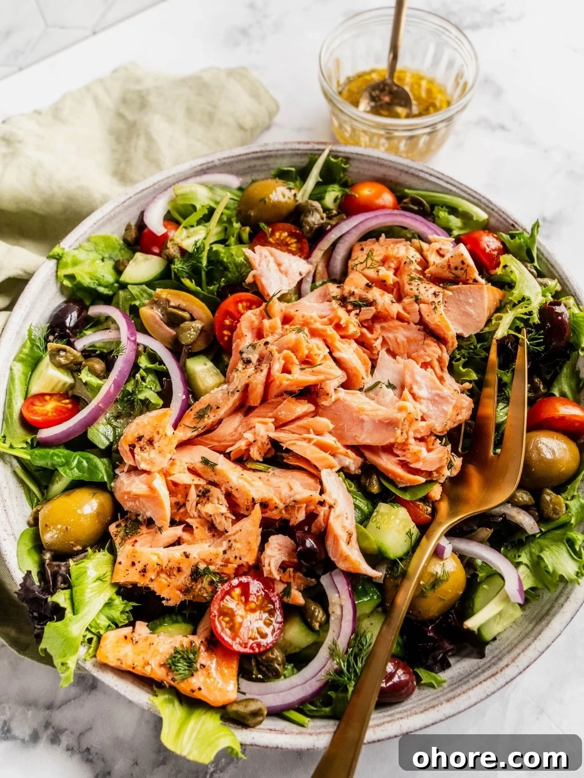 Mediterranean Salmon Salad bowl with flaky salmon over a bed of greens, tomatoes, olives and cucumbers.