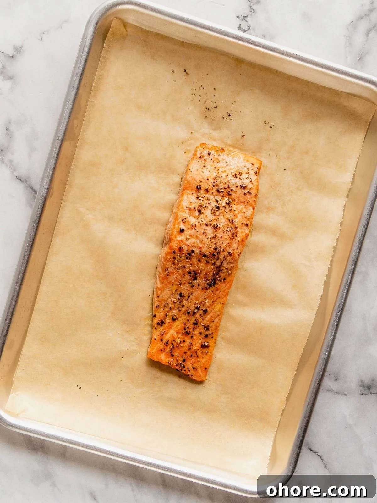 A cooked salmon filet on a parchment paper-lined baking sheet.