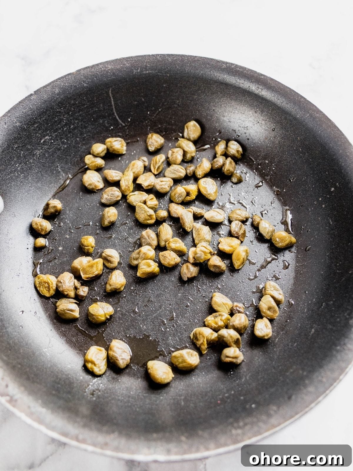 Capers frying in a small frying pan.