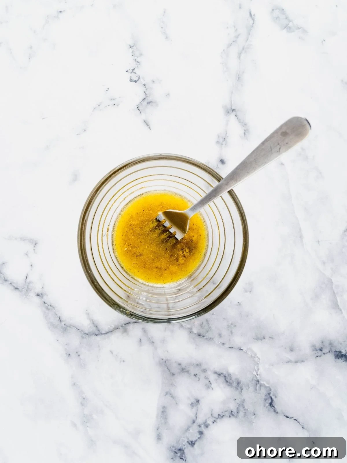 A small bowl with olive oil, lemon juice, mustard and seasoning.