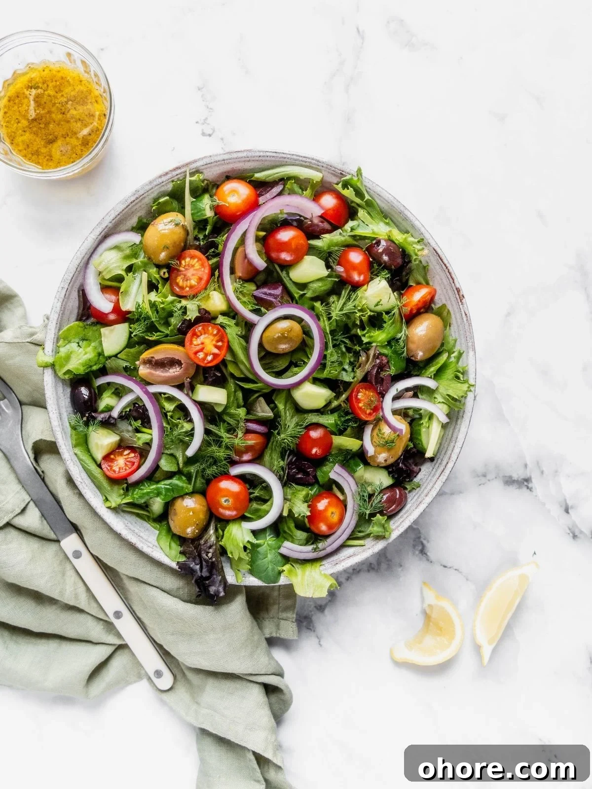A bowl of mixed greens, sliced onion, cherry tomatoes, cucumbers and olives.