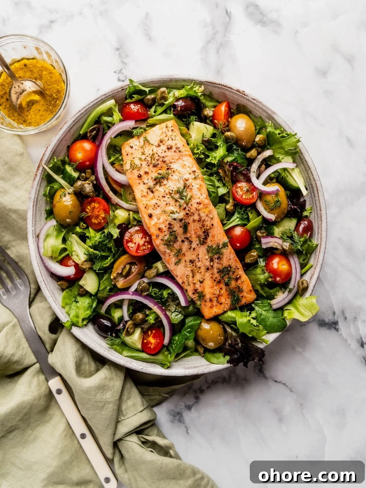 Mediterranean Salmon Salad bowl with flaky salmon over a bed of greens, tomatoes, olives and cucumbers.
