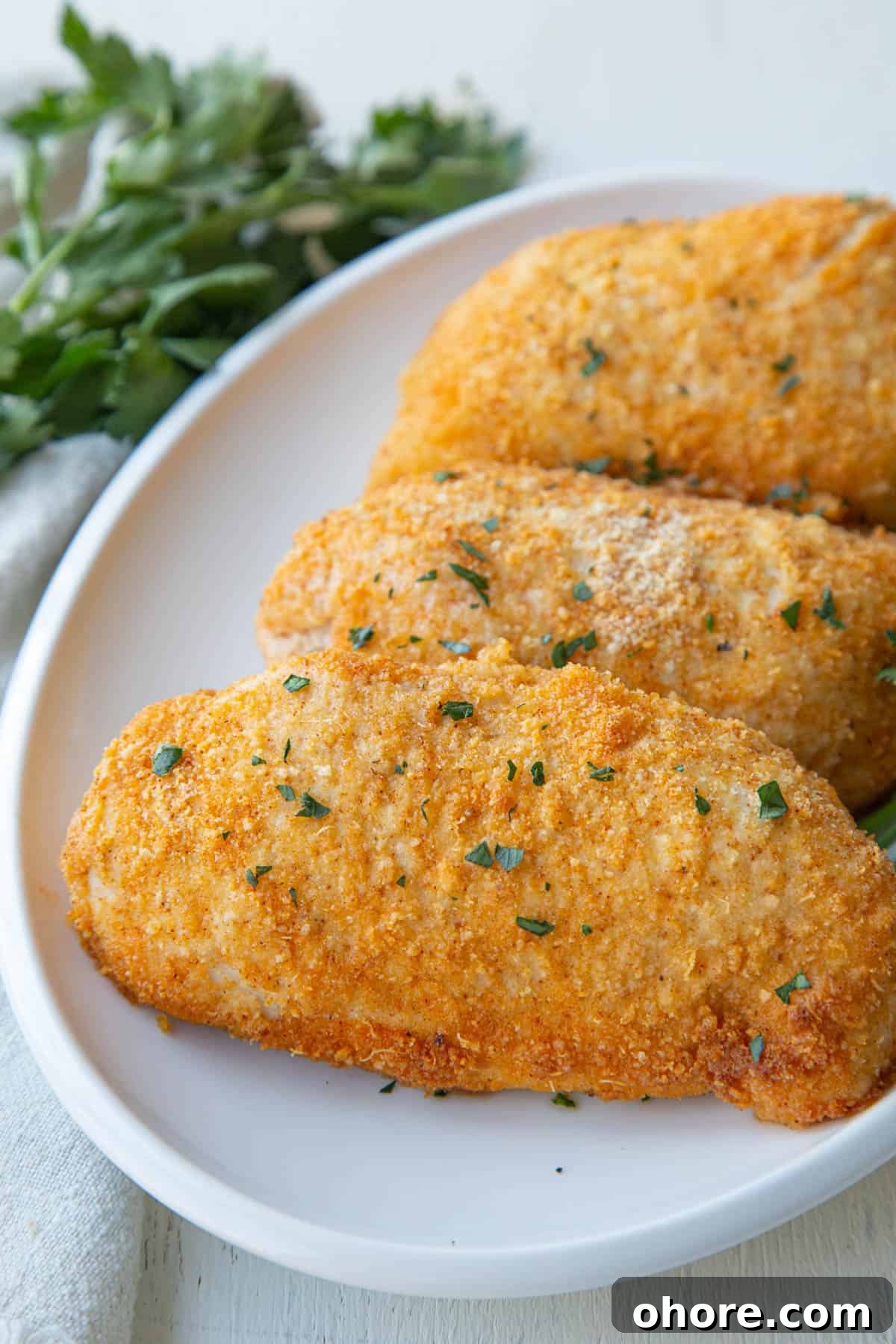 Crispy Parmesan-Crusted Baked Chicken Breast Recipe 2 baked parmesan crusted chicken breasts on a white platter.