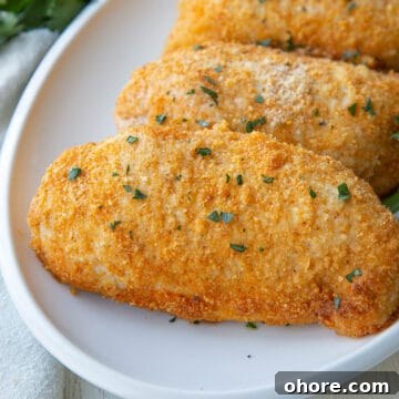 Crispy Parmesan-Crusted Baked Chicken Breast Recipe 9 baked parmesan crusted chicken breasts on a white platter.