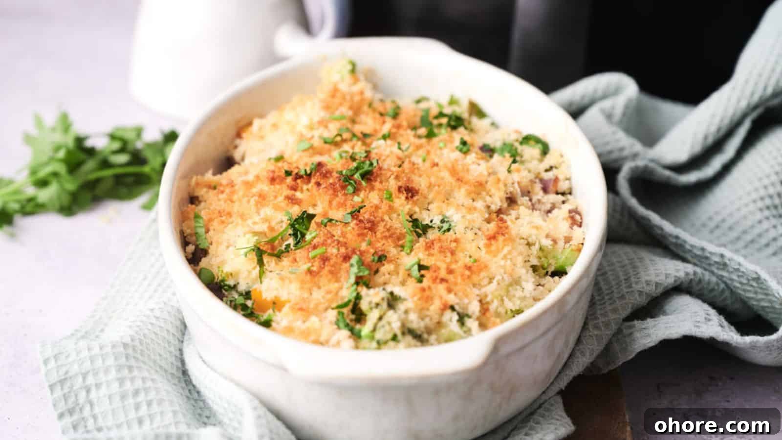 29 Cozy Air Fryer Casseroles for Warm January Dinners 11 A white ceramic dish containing baked vegetable gratin topped with browned breadcrumbs and parsley, placed on a light green textured cloth.