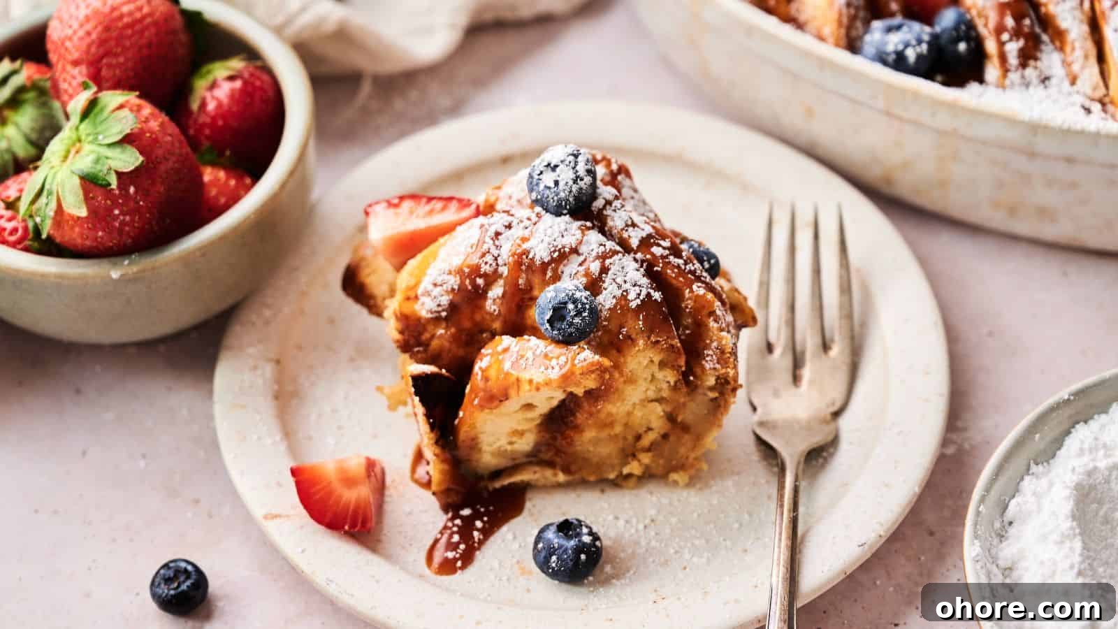 29 Cozy Air Fryer Casseroles for Warm January Dinners 26 A serving of French toast casserole topped with blueberries, strawberries, and powdered sugar sits on a plate next to a fork; a bowl of fresh strawberries is nearby.