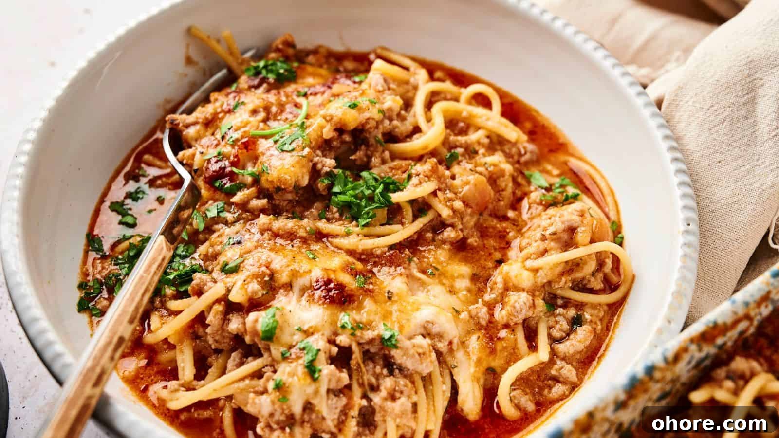 29 Cozy Air Fryer Casseroles for Warm January Dinners 30 A bowl of spaghetti topped with meat sauce, melted cheese, and chopped parsley, with a fork resting inside.