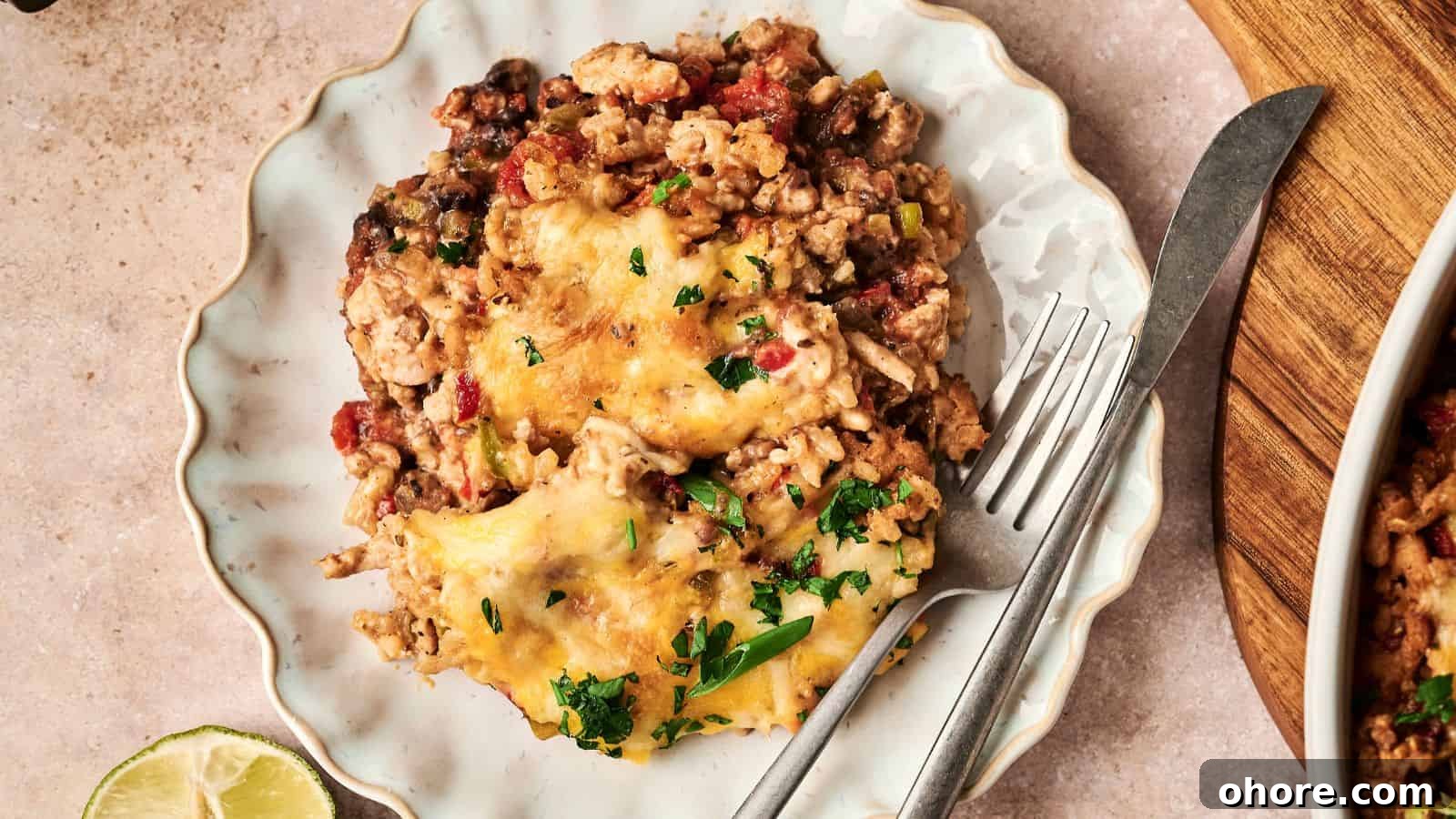29 Cozy Air Fryer Casseroles for Warm January Dinners 6 A plate with a serving of cheesy casserole containing ground meat, beans, and chopped herbs, accompanied by a fork and knife. A lime wedge is partially visible on the side.