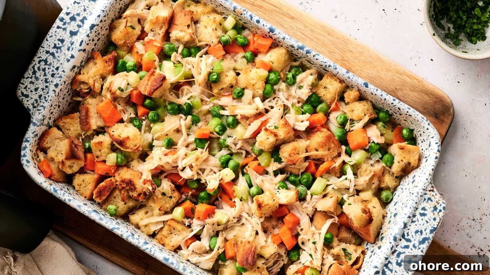29 Cozy Air Fryer Casseroles for Warm January Dinners 10 A casserole dish filled with baked bread cubes, shredded chicken, peas, carrots, and celery, arranged on a wooden board.