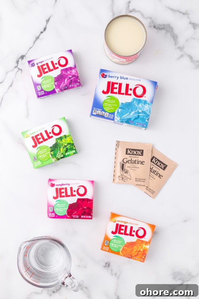 Retro Broken Glass Jello Recipe – Colorful Layered Dessert 3 Ingredients for Broken Glass Jello recipe including colorful Jello boxes, sweetened condensed milk, Knox gelatin, and measuring cup on marble background