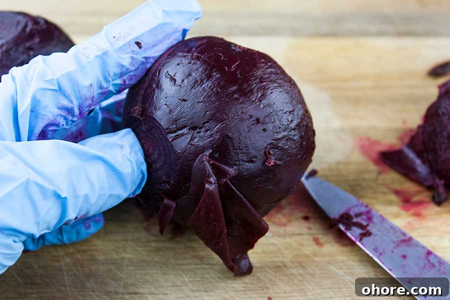 Ninja Foodi Pressure Cooker Fresh Beets - Fresh beets in 30 minutes! So flavorful, tender and healthy! A beautiful colorful side dish to any meal. Gloved hand holding cooked beet removing the skin with a paring knife.