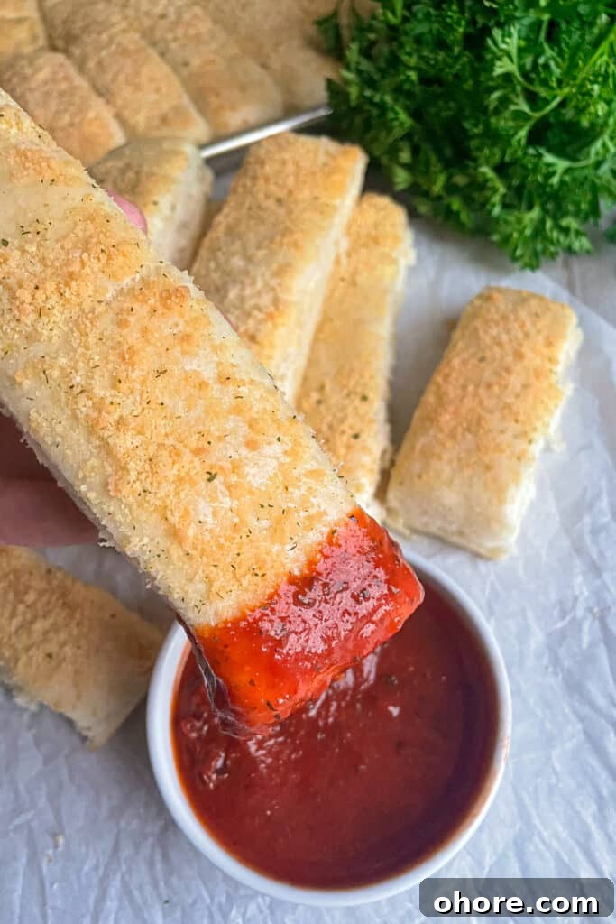 Parmesan Garlic Breadsticks: Homemade Recipe in 30 Minutes 3 Close up shot of an individual quick and easy homemade breadstick dipped in marinara sauce