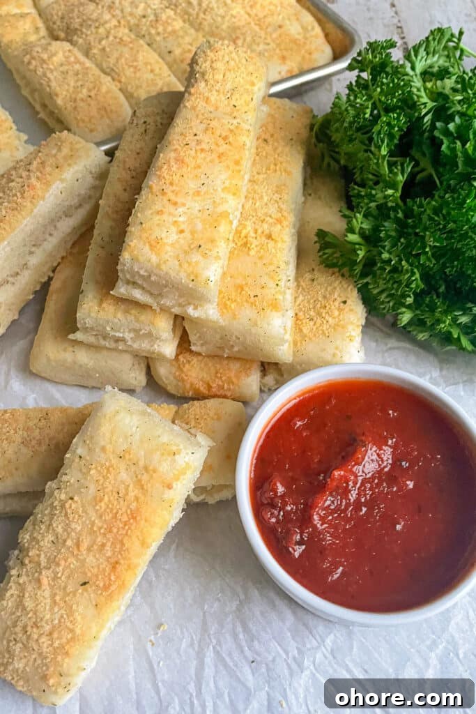 Parmesan Garlic Breadsticks: Homemade Recipe in 30 Minutes 5 easy homemade breadsticks stacked on top of eachother and a white container of marinara sauce