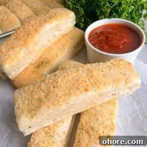 Parmesan Garlic Breadsticks: Homemade Recipe in 30 Minutes 6 easy homemade breadsticks stacked on top of eachother and a white container of marinara sauce