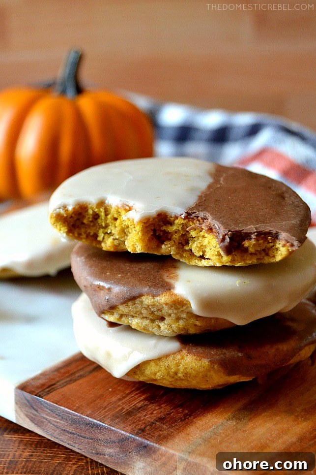 Bitten black and white pumpkin cookie stacked on wooden board with a pumpkin