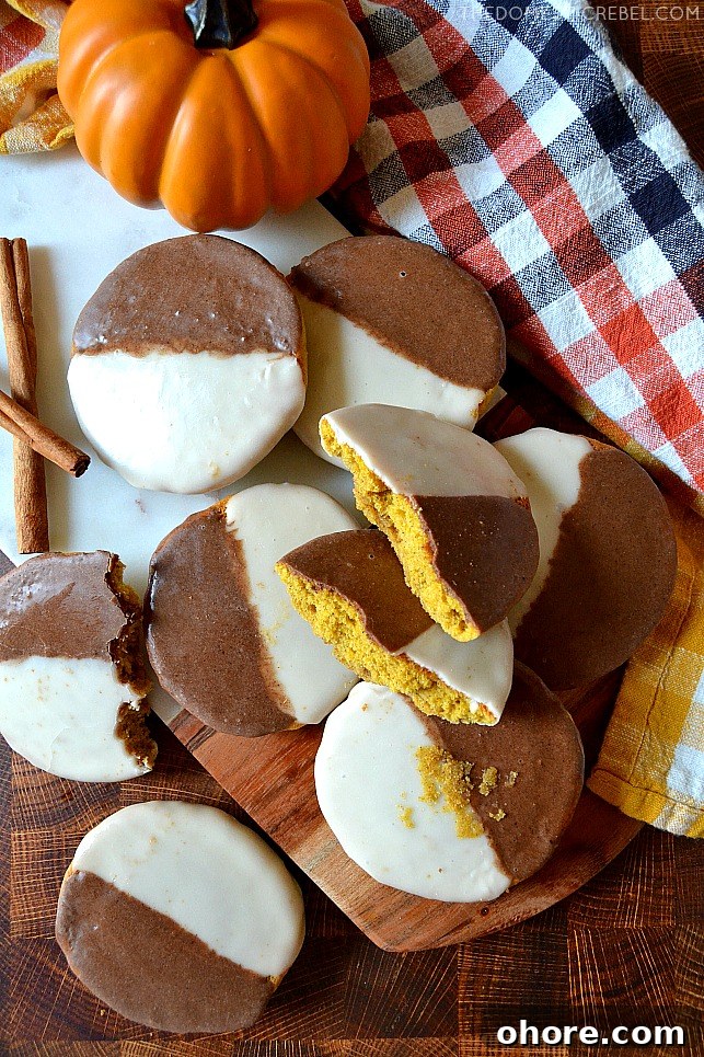 Scattered arrangement of pumpkin black and white cookies on a wooden cutting board