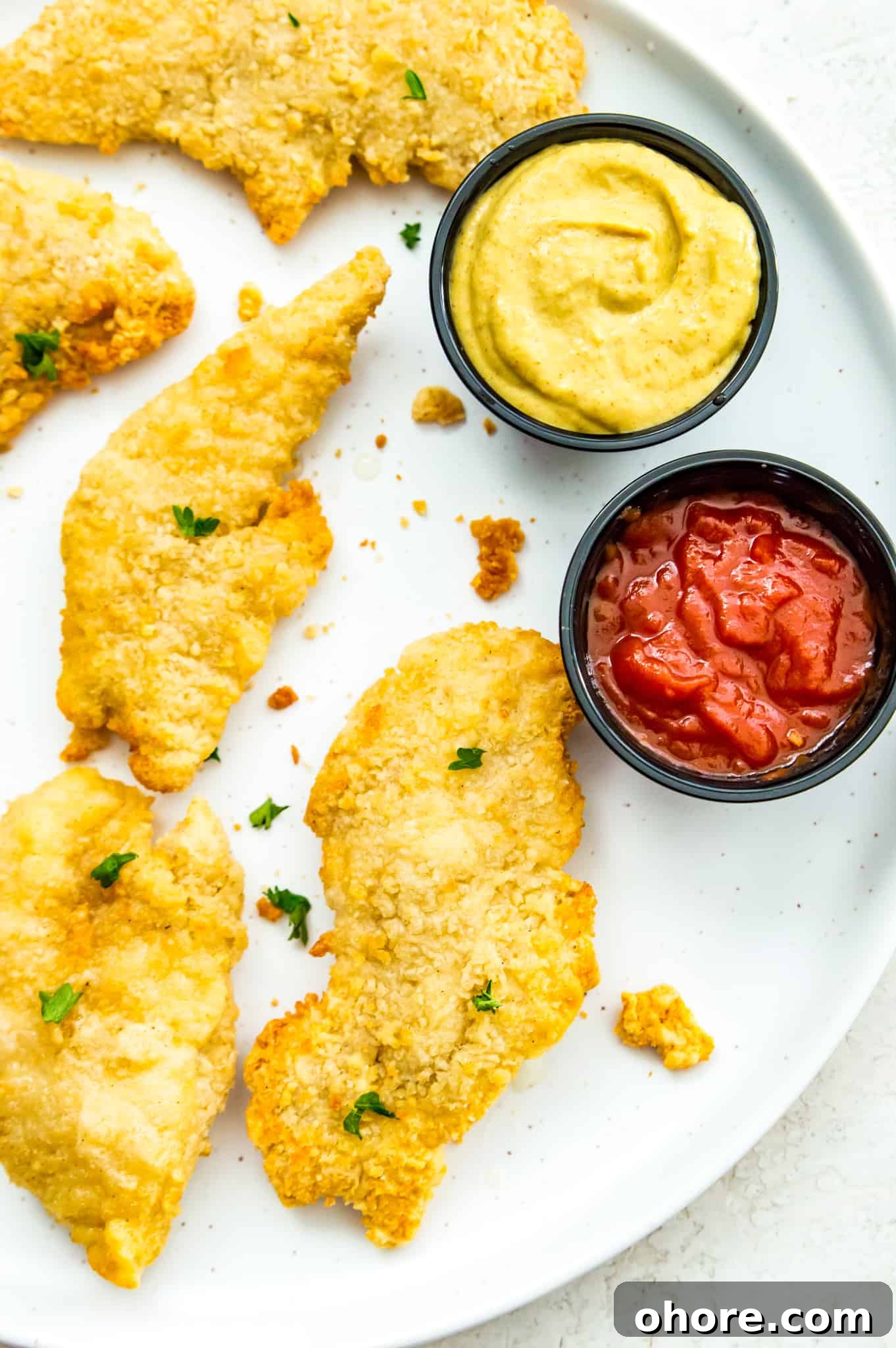 cooked chicken tenders A plate of cooked chicken tenders with a side of ketchup and mustard.