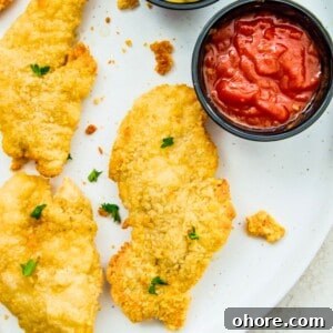 Crispy Air Fryer Frozen Chicken Tenders in 15 Minutes 7 Cooked chicken tenders on a plate with a dish full of ketchup beside them.