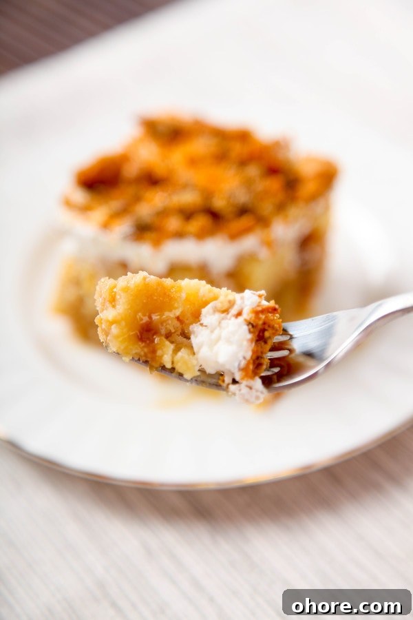 a closeup of one bite of butterfinger cake on a fork with a slice of cake in the background.