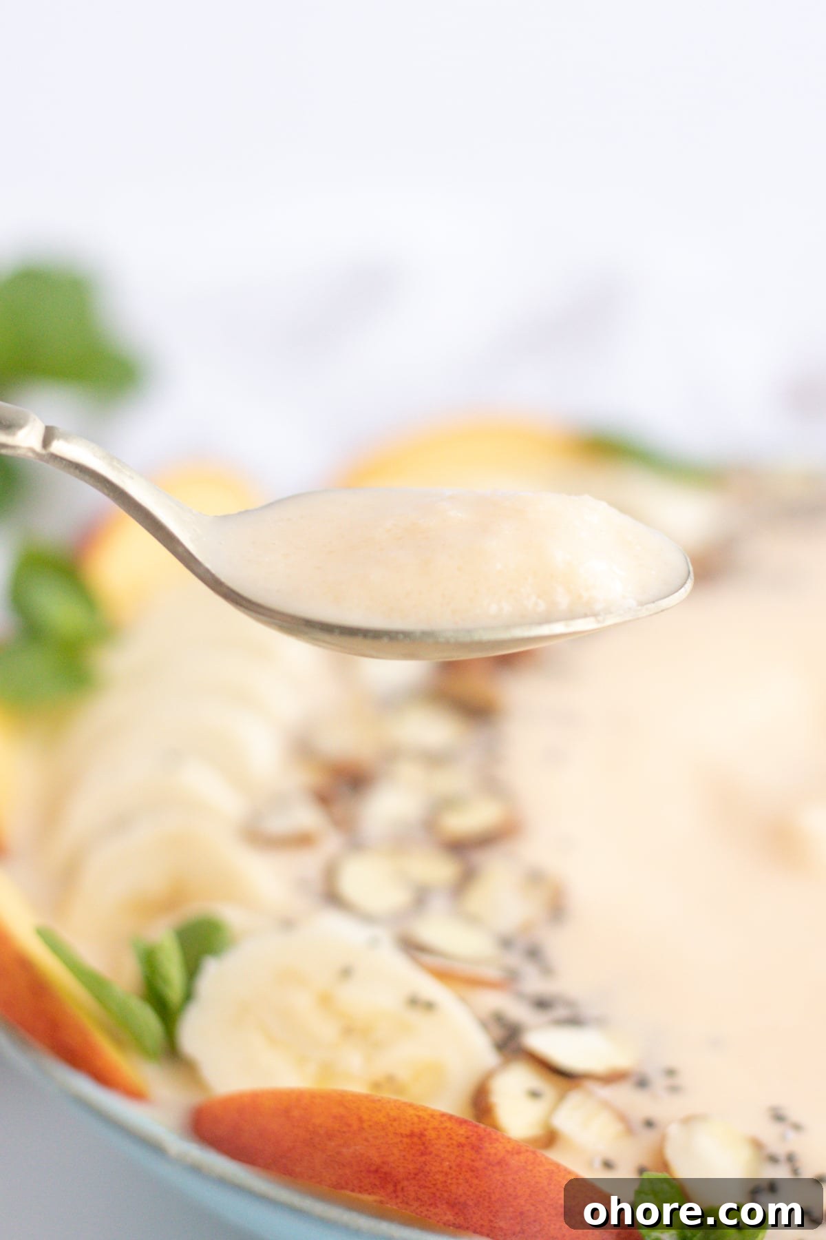 up close shot of spoon with peach smoothie and bowl in the background