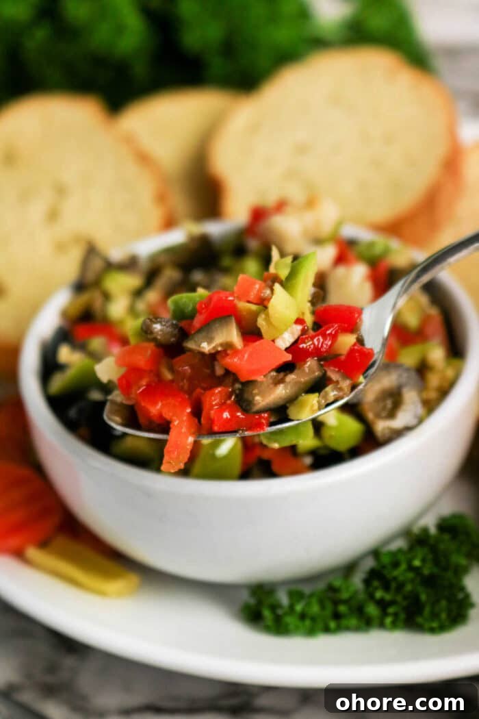 Authentic Muffuletta Olive Salad Recipe for Classic Sandwiches 5 A spoonful of mixed chopped vegetables above a bowl, hinting at a classic Olive Salad recipe, with bread slices in the background.