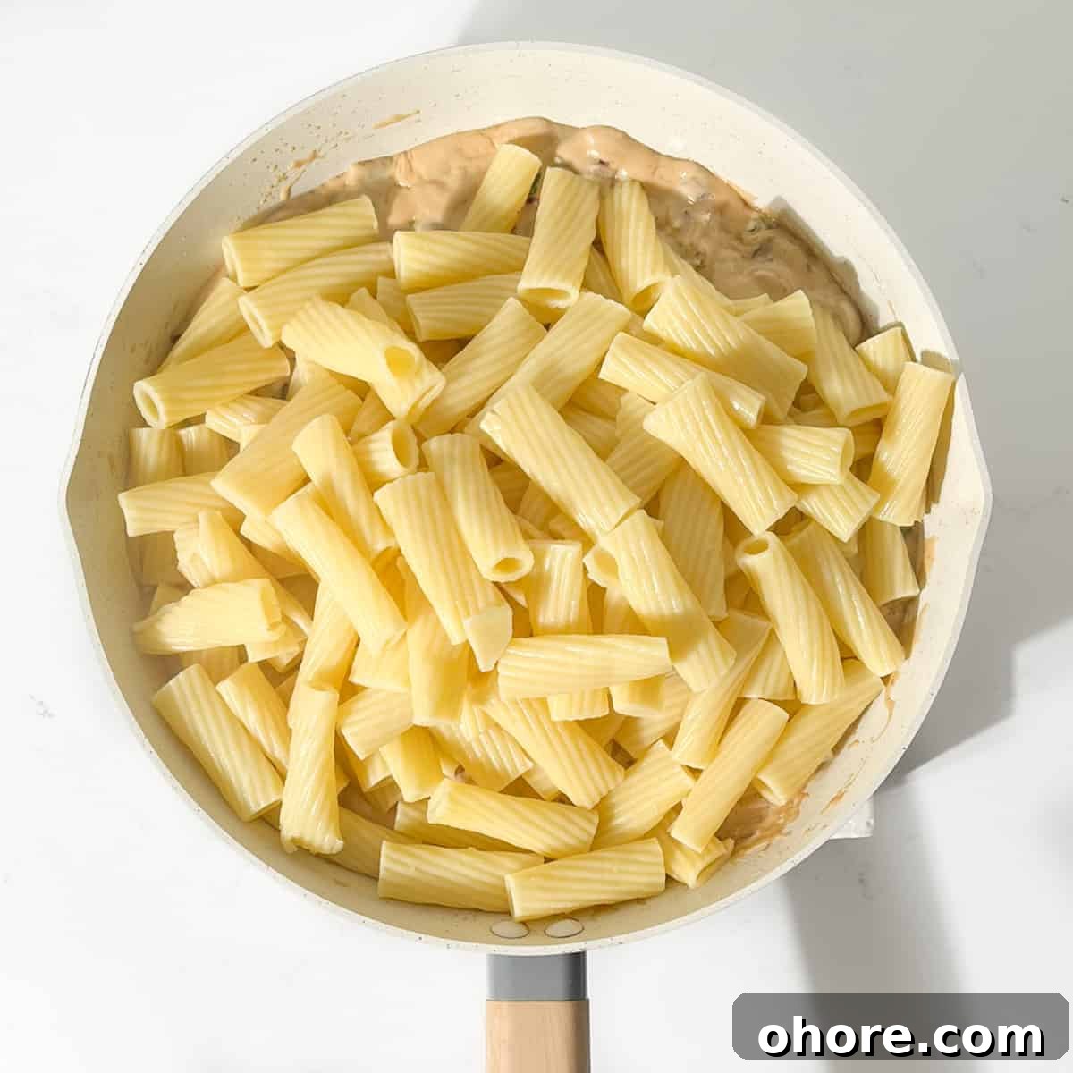 Adding the pasta to the sauce in a large frying pan.
