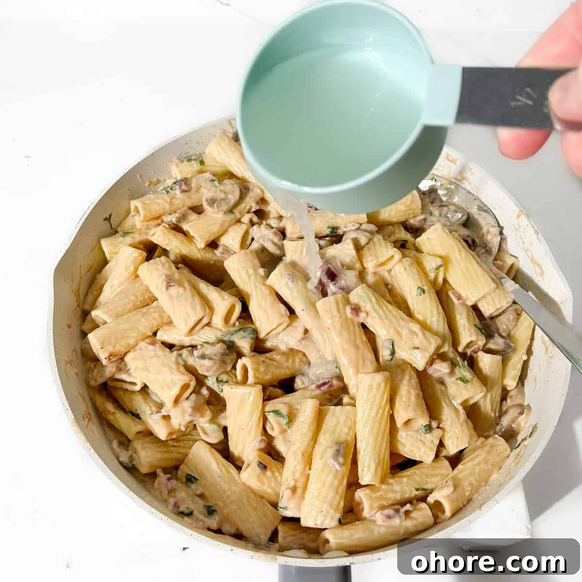 Adding the reserved pasta water to the creamy steak pasta.