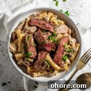 A bowl of creamy steak pasta on a white background.