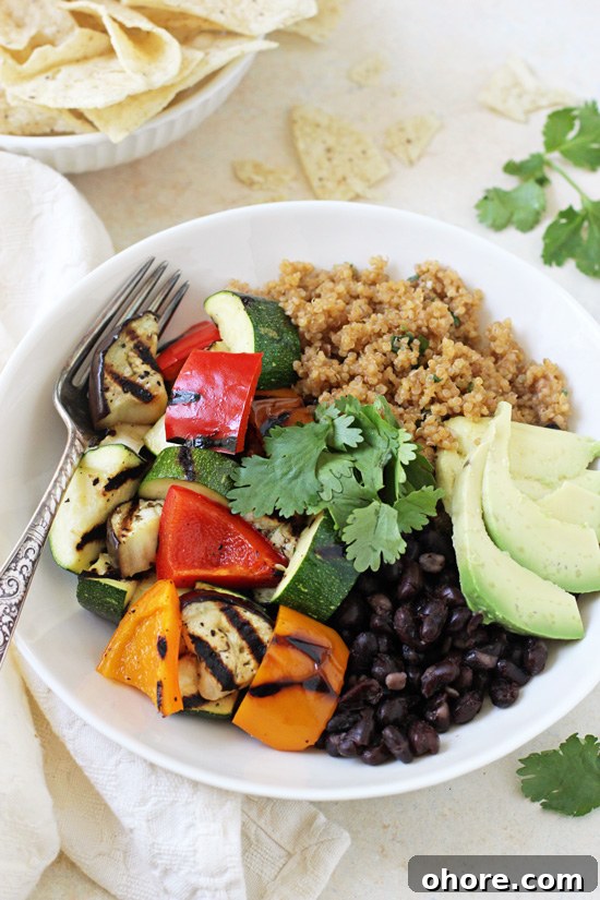 These easy and delicious grilled vegetable enchilada bowls are perfect for the season! With grilled veggies, quinoa pilaf and fun toppings! Side angle view of a Grilled Vegetable Enchilada Bowl with a fork and a bowl of tortilla chips in the background.
