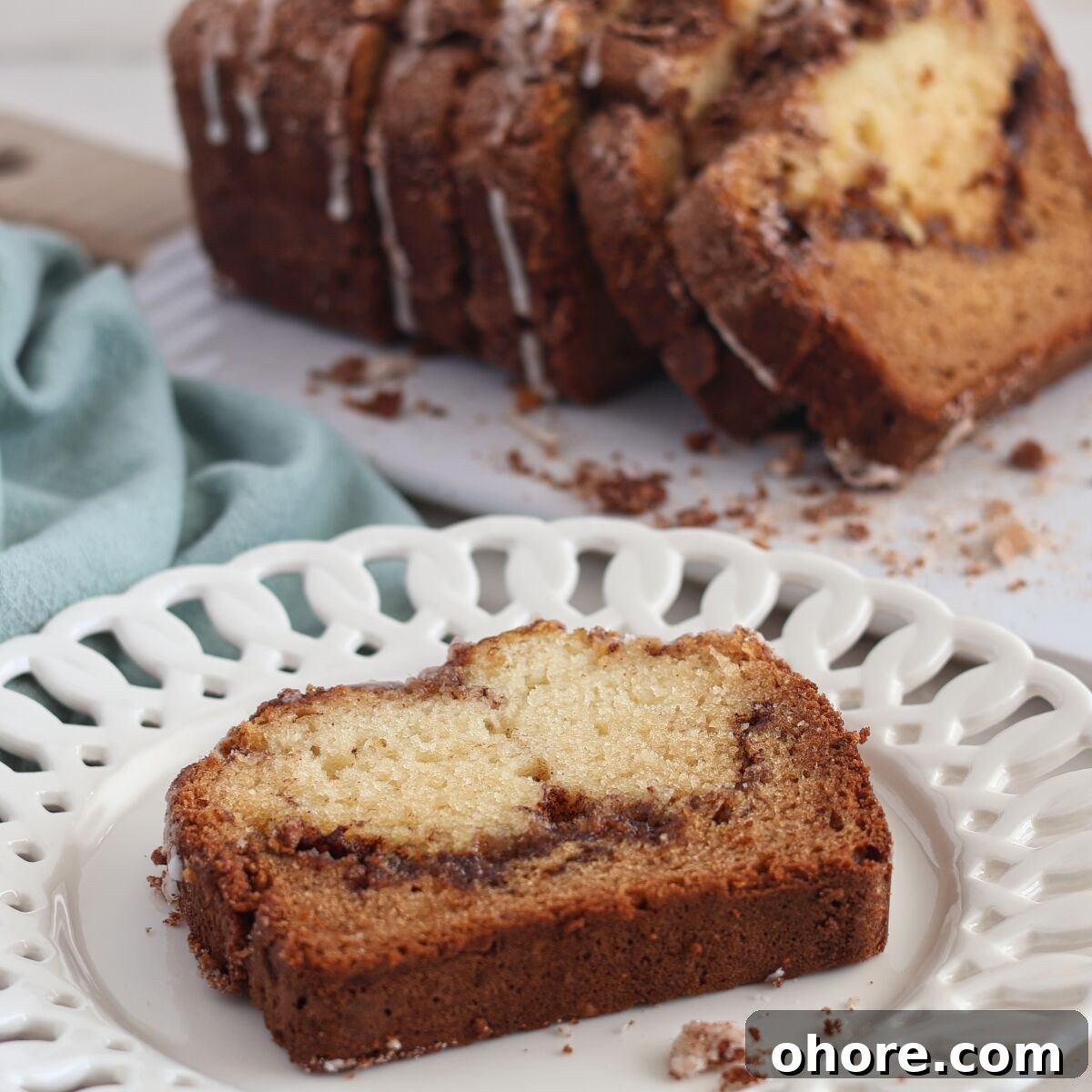 slice of cinnamon bread on white scalloped plate with whole loaf sliced in the background.
