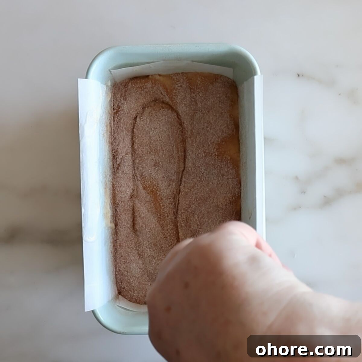 swirling cinnamon sugar topping in loaf pan with a butter knife.