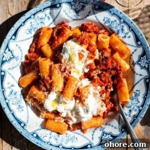 A close up of spicy calabrian sausage ragu in a blue and white bowl with stracciatella on top