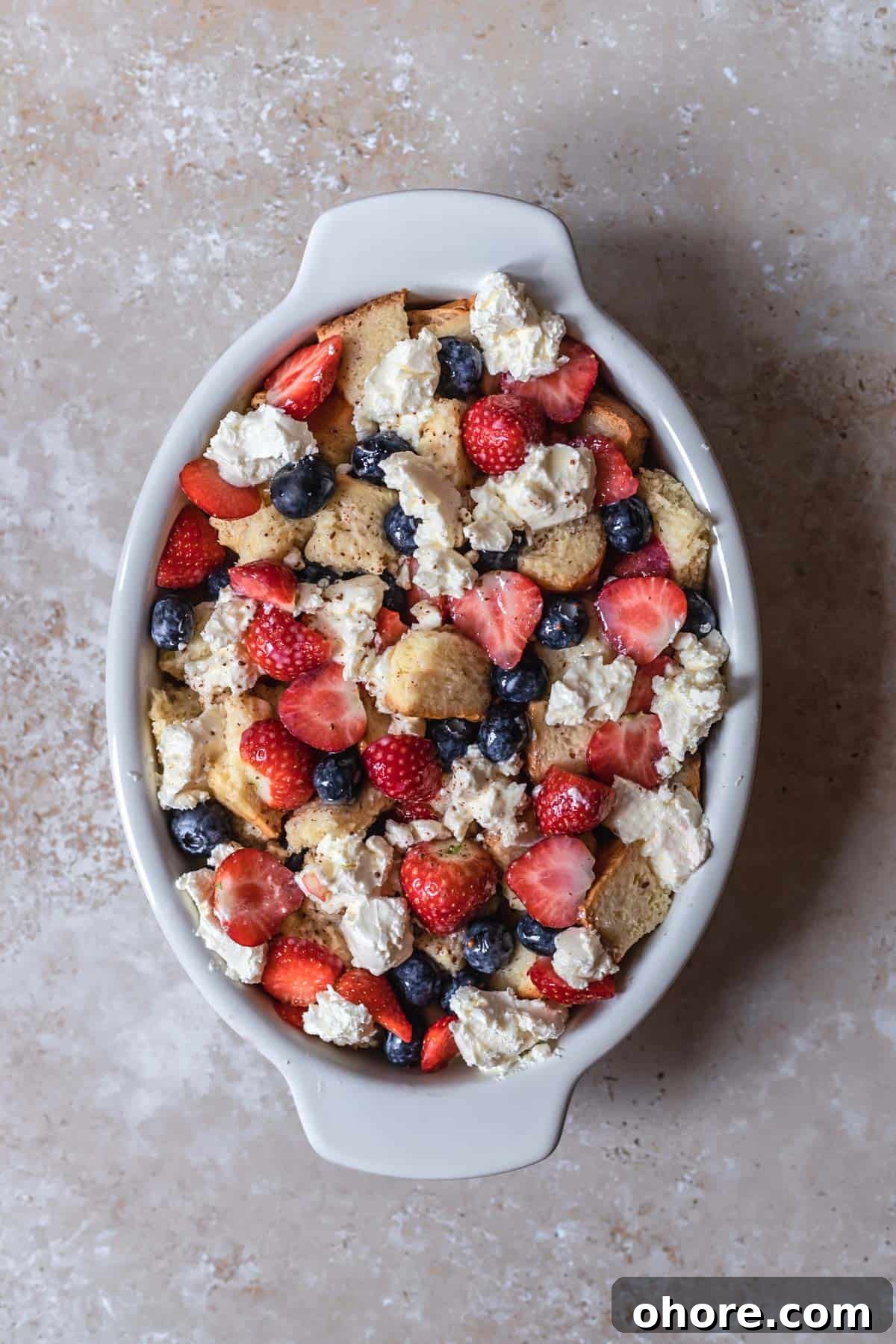 Berry Brioche Cream Cheese French Toast Bake for Brunch 7 bread pieces, sliced strawberries, blueberries, and cream cheese in an oval baking dish