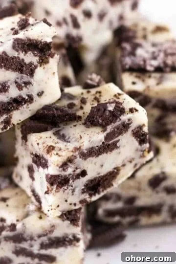 Creamy Oreo fudge stacked on a white serving plate, with chunks of cookie showing through.