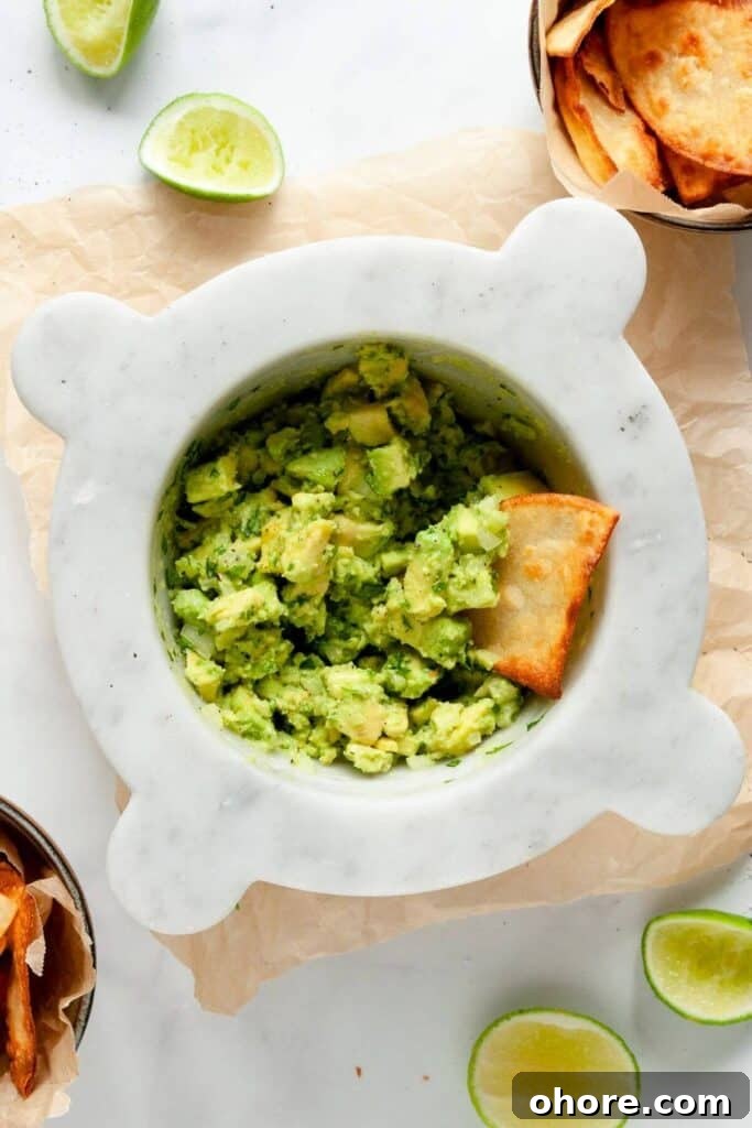 Bowl of chunky 4 ingredient guacamole with a crispy homemade tortilla chip dipped in it