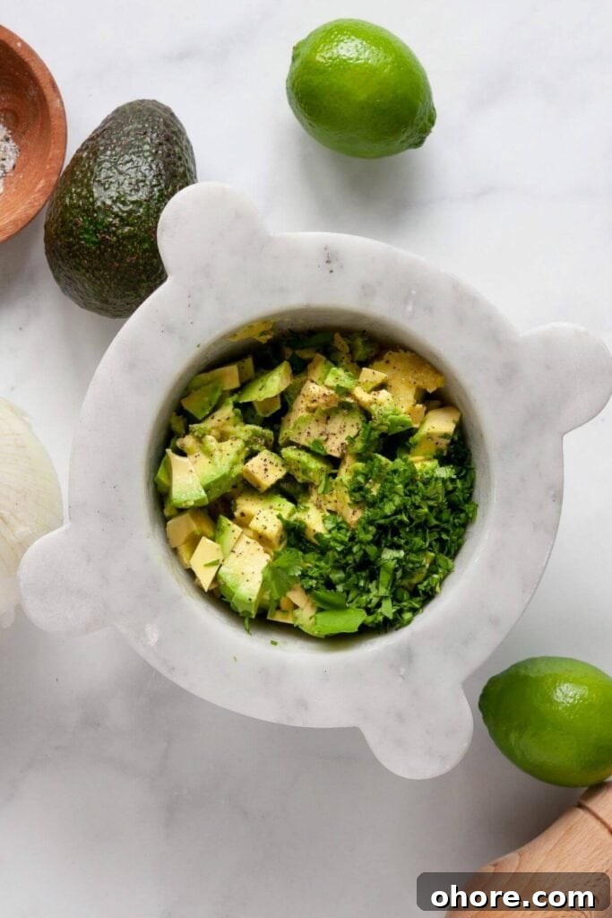 Fresh avocados, onion, cilantro, and lime juice in a bowl ready to be mashed