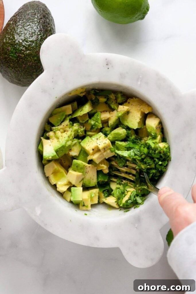 Mashing diced avocado with a fork in a bowl along with other guacamole ingredients