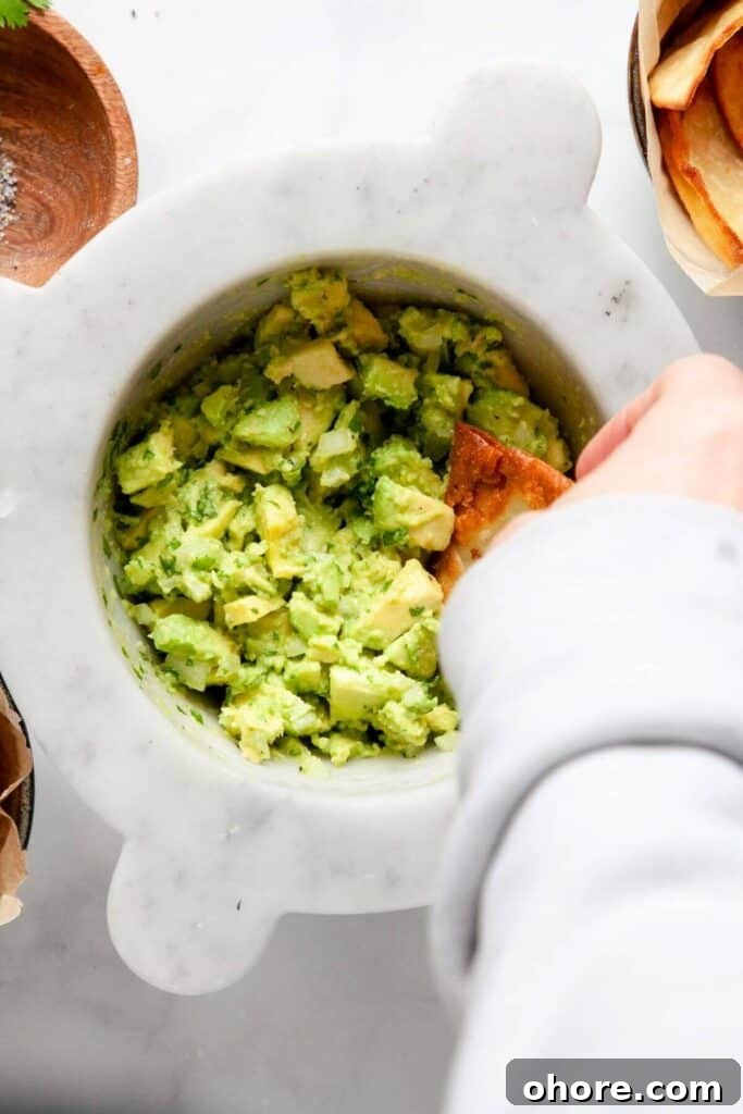 Crunchy tortilla chip scooping chunky guacamole made with four simple ingredients