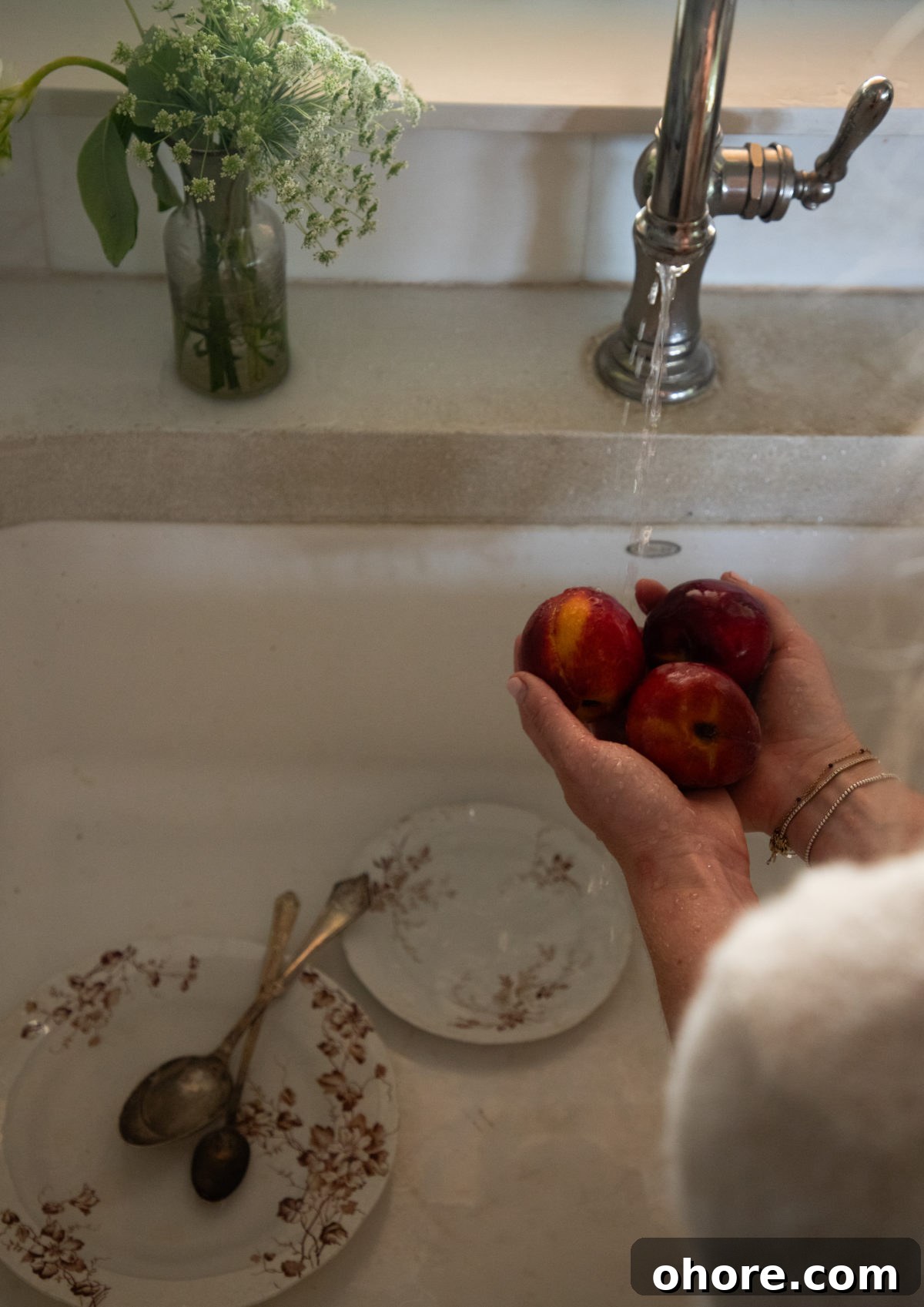 Ultimate Homemade Peach Cake Recipe for Moist, Fruity Perfection 2 woman's hands holding 3 peaches above a sink with brown floral dishes in the sink below