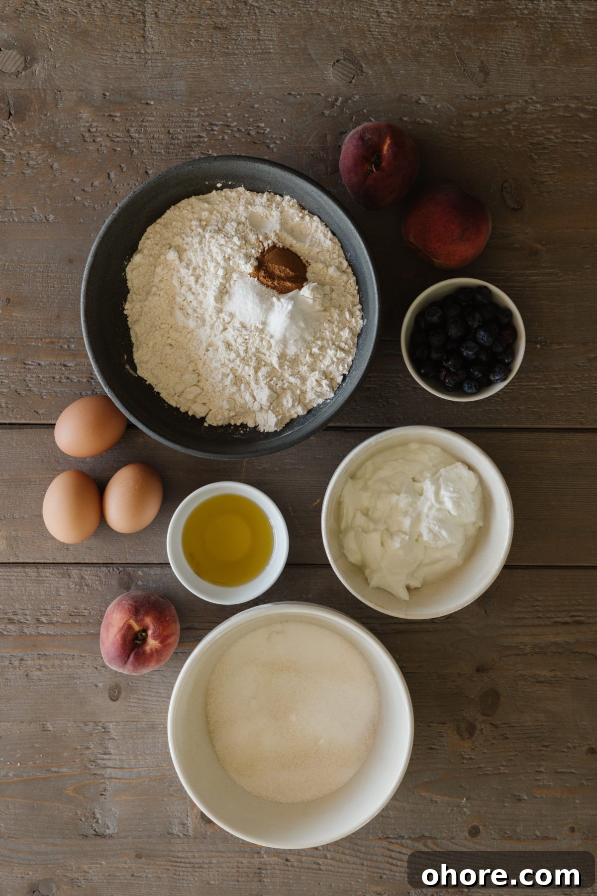 Ultimate Homemade Peach Cake Recipe for Moist, Fruity Perfection 4 peach cake ingredients in various neutral colored bowls, 3 brown eggs, and some peaches on a rustic wooden table top
