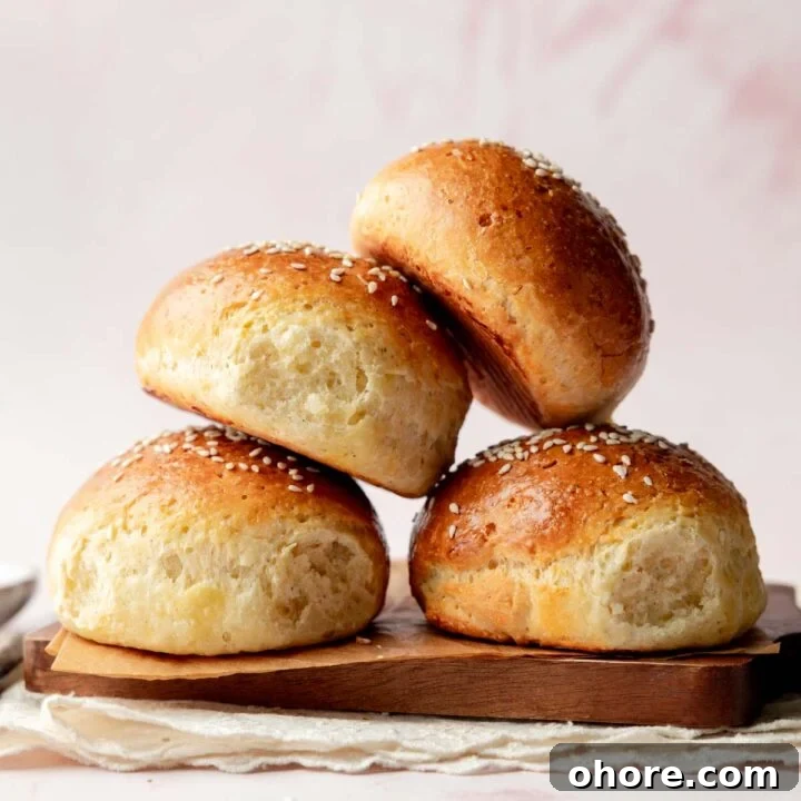 Side view of a stack of fluffy gluten-free hamburger buns with shiny, golden crusts and sesame seed topping.