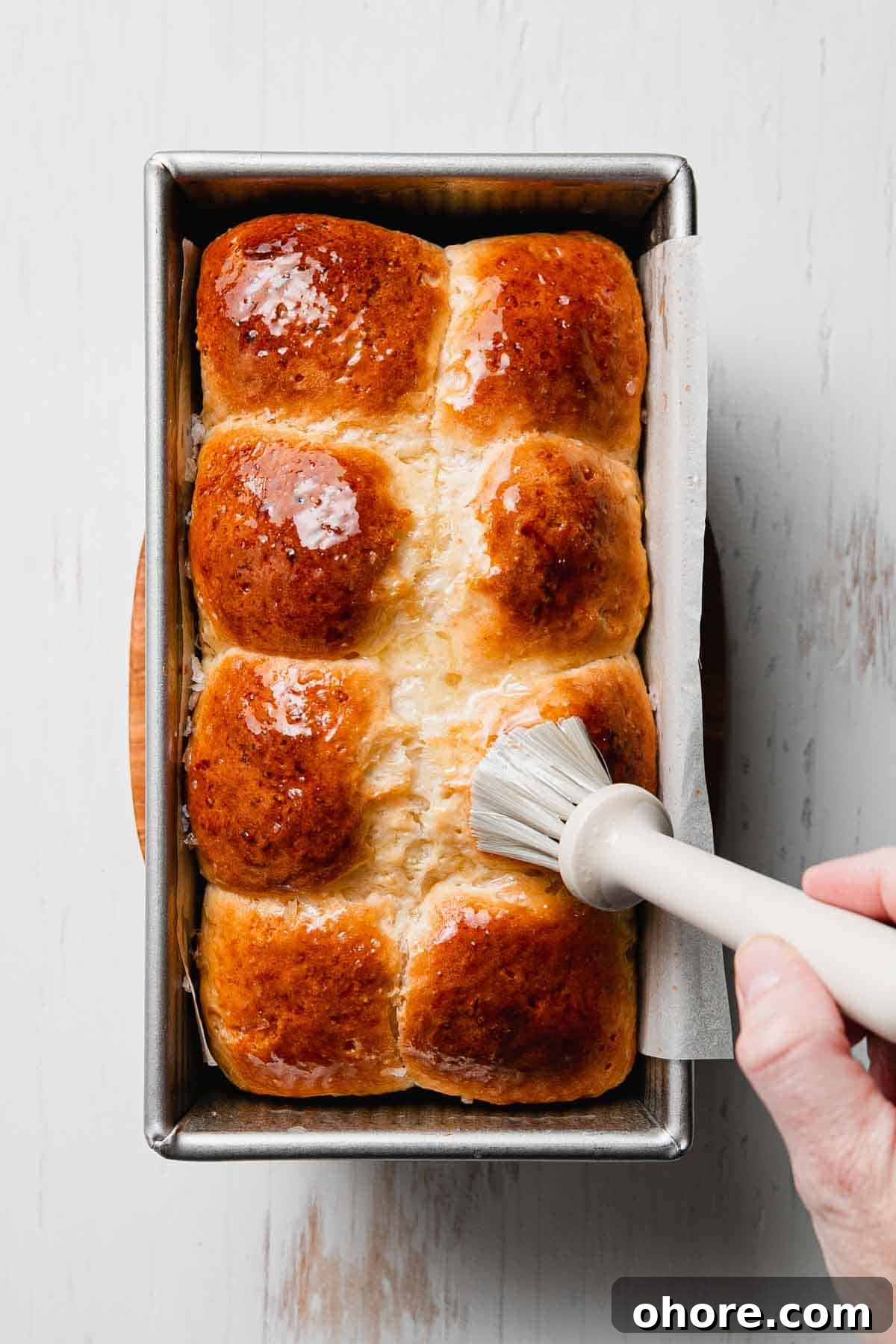 Soft Gluten-Free Dinner Rolls Recipe — Classic Homemade Rolls 8 Brushing butter on top of golden brown rolls in a loaf pan.