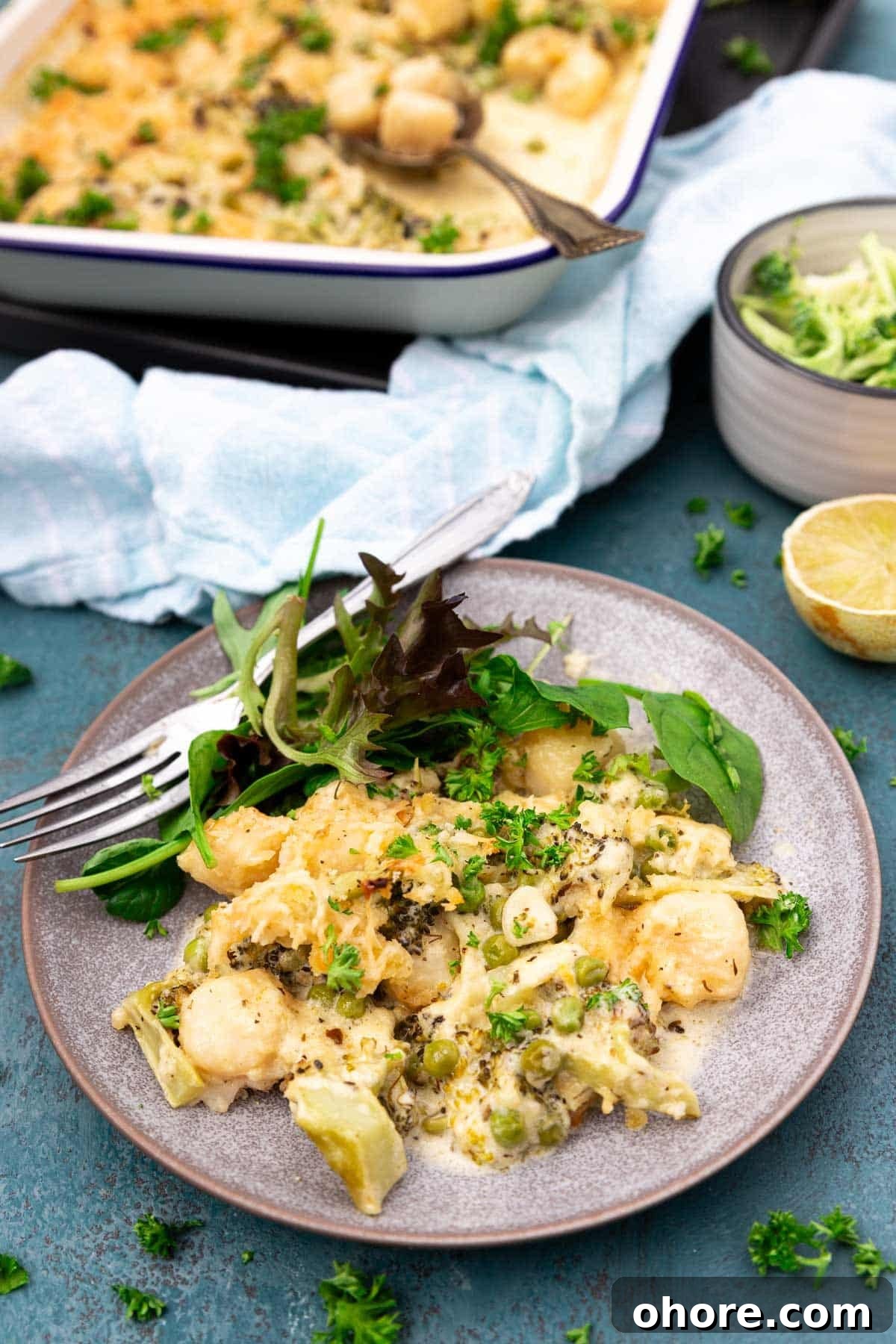 One-Pan Baked Creamy Broccoli Gnocchi Recipe 2 A blue plate of baked broccoli gnocchi with green salad and a fork, and with the baking dish in the background.