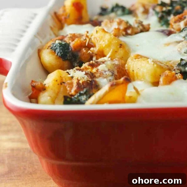 One-Pan Baked Creamy Broccoli Gnocchi Recipe 13 Closeup of a red baking dish of butternut squash gnocchi with sausage and kale on a wooden board.