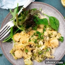 One-Pan Baked Creamy Broccoli Gnocchi Recipe 14 A blue plate of baked broccoli gnocchi with green salad and a fork, and with a pale blue tea towel at the top.