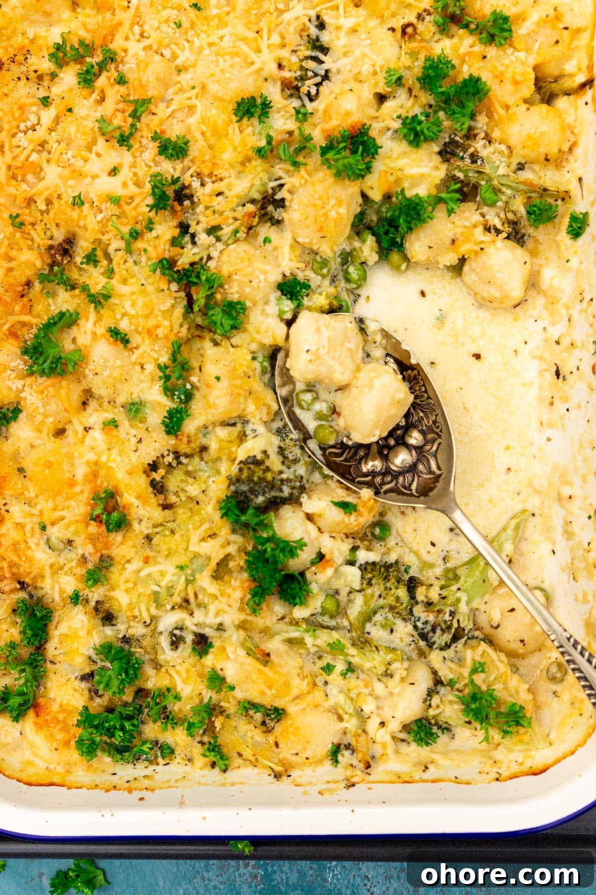One-Pan Baked Creamy Broccoli Gnocchi Recipe 8 Closeup view of the top of a white baking dish of baked broccoli gnocchi with a decorative spoon in it.