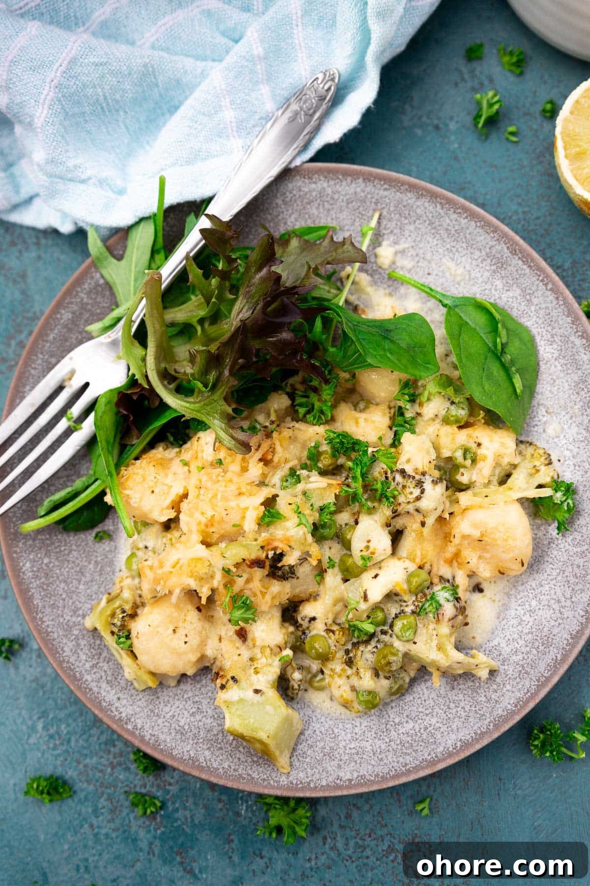 One-Pan Baked Creamy Broccoli Gnocchi Recipe 9 A blue plate of baked broccoli gnocchi with green salad and a fork, and with a pale blue tea towel at the top.