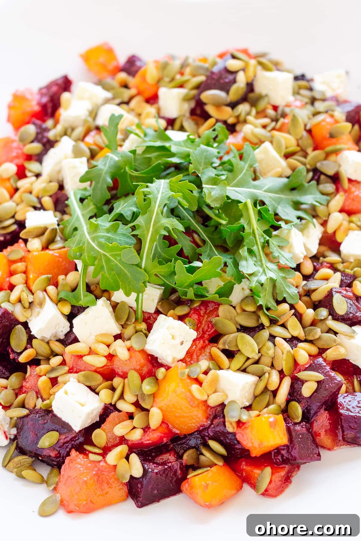 Roasted Pumpkin and Beetroot Salad with Feta and Toasted Seeds 8 Close up photo of roasted pumpkin and beetroot salad topped with feta cheese, pine nuts, pepitas and arugula.