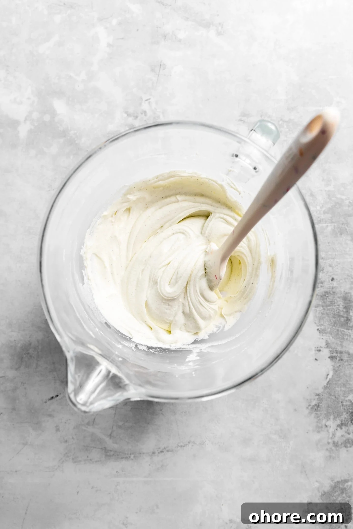 Cream Cheese Frosting with 5 Simple Ingredients 6 Cream cheese frosting inside of a clear bowl with a silicone spatula.