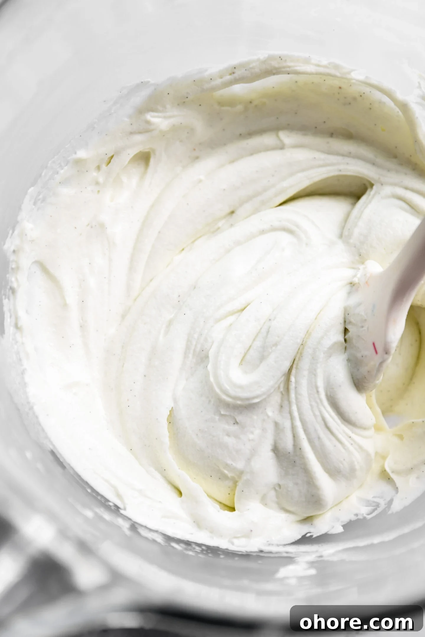 Cream Cheese Frosting with 5 Simple Ingredients 7 Close up of smooth cream cheese frosting and a silicone spatula inside a clear mixing bowl.